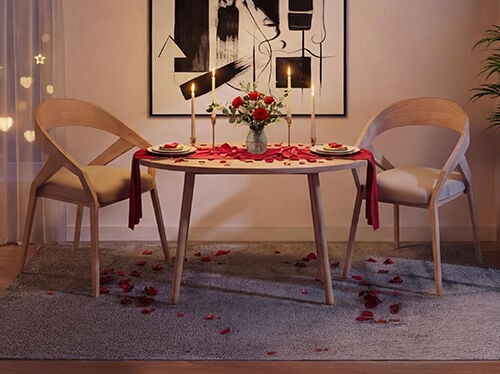 Ensemble de table &agrave; manger romantique pour deux dans un salon cosy, avec une table ronde en bois et des chaises modernes assorties, une douce lueur de bougies, un vase de roses rouges, des p&eacute;tales de rose &eacute;parpill&eacute;s sur la table et le sol, et un &eacute;clairage d&rsquo;ambiance chaleureux cr&eacute;ant une atmosph&egrave;re intime de Saint-Valentin.