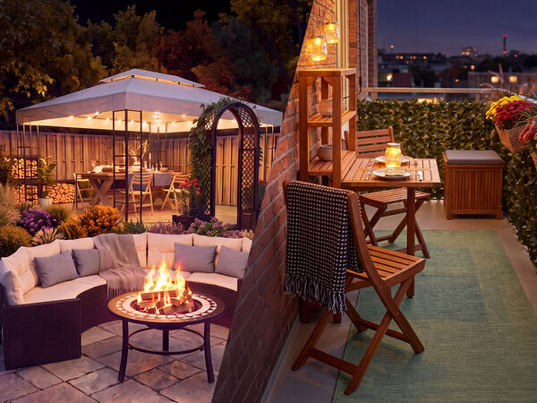 Espaces de vie ext&eacute;rieurs cosy au cr&eacute;puscule, avec un salon de jardin et un brasero d&rsquo;un c&ocirc;t&eacute;, ainsi qu&rsquo;une tonnelle fleurie, et de l&rsquo;autre, un balcon d&eacute;cor&eacute; avec mobilier en bois, &eacute;clairage par lanternes et fleurs en pot donnant sur un panorama urbain.