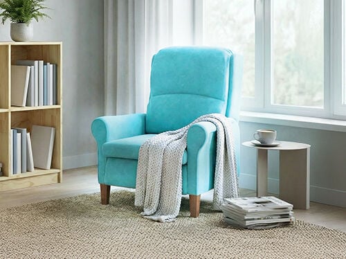 Fauteuil turquoise pr&egrave;s d&rsquo;une fen&ecirc;tre, avec un plaid, une table d&rsquo;appoint et des livres empil&eacute;s dans un espace lumineux et chaleureux